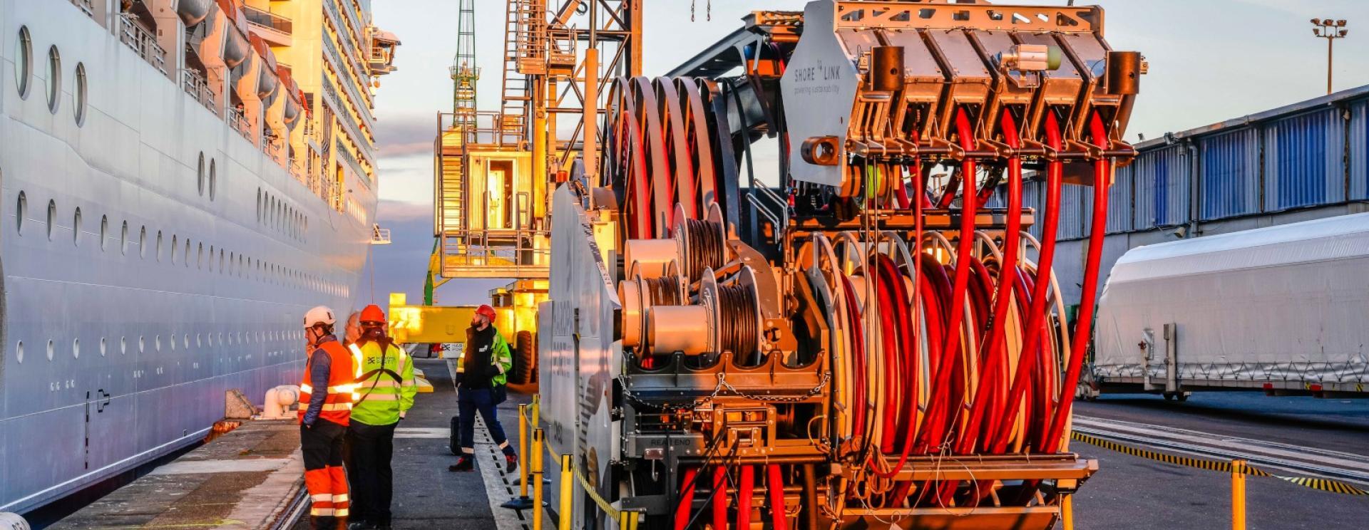 Groupe de personnes opérant le branchement électrique du navire MSC Poesia au quai Pierre Callet du Havre grâce à l'utilisation d'un véhicule équipé de bras articulés et de câbles. 