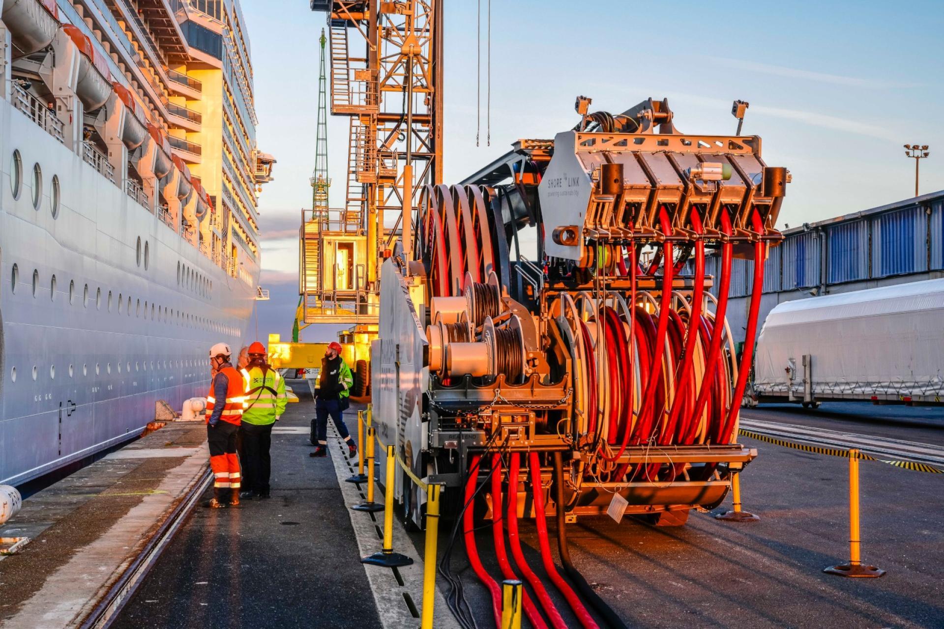 Groupe de personnes opérant le branchement électrique du navire MSC Poesia au quai Pierre Callet du Havre grâce à l'utilisation d'un véhicule équipé de bras articulés et de câbles. - Agrandir l'image, fenêtre modale